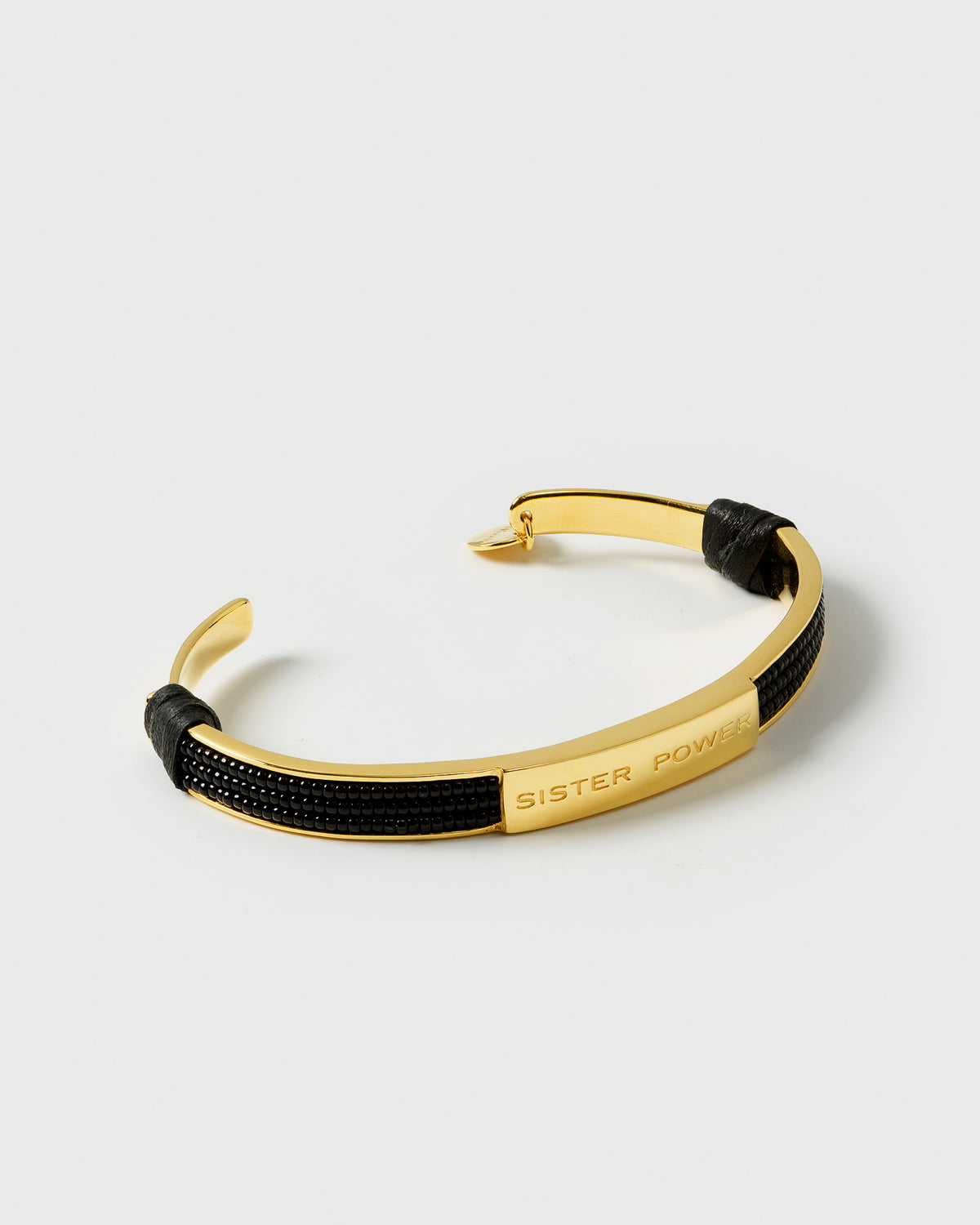 A product shot of the Sister Power Bracelet in gold, a cuff bangle adorned with black beads and engraved with the words 'SISTER POWER'.