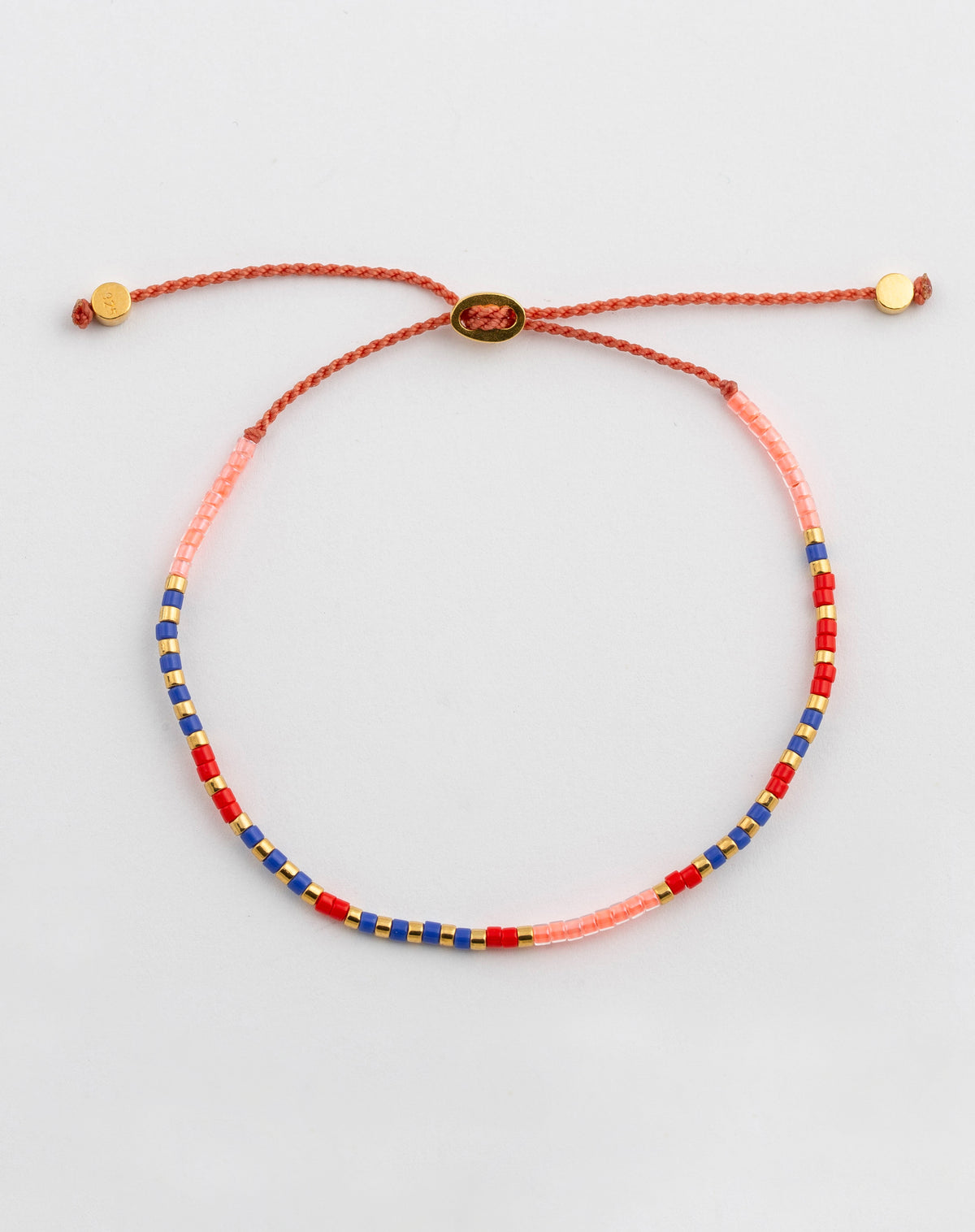 A product shot of the Code Bracelet Gold 'Just Breathe', laid out to display its multicolored beads in pink, red, blue, and gold, which spell out the message in Morse code on an adjustable cord.