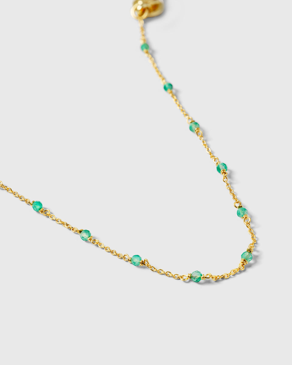 A product shot of the Santa Monica Bracelet in gold, showing a close-up of the fine chain detailed with small, vibrant green onyx stones spaced throughout.