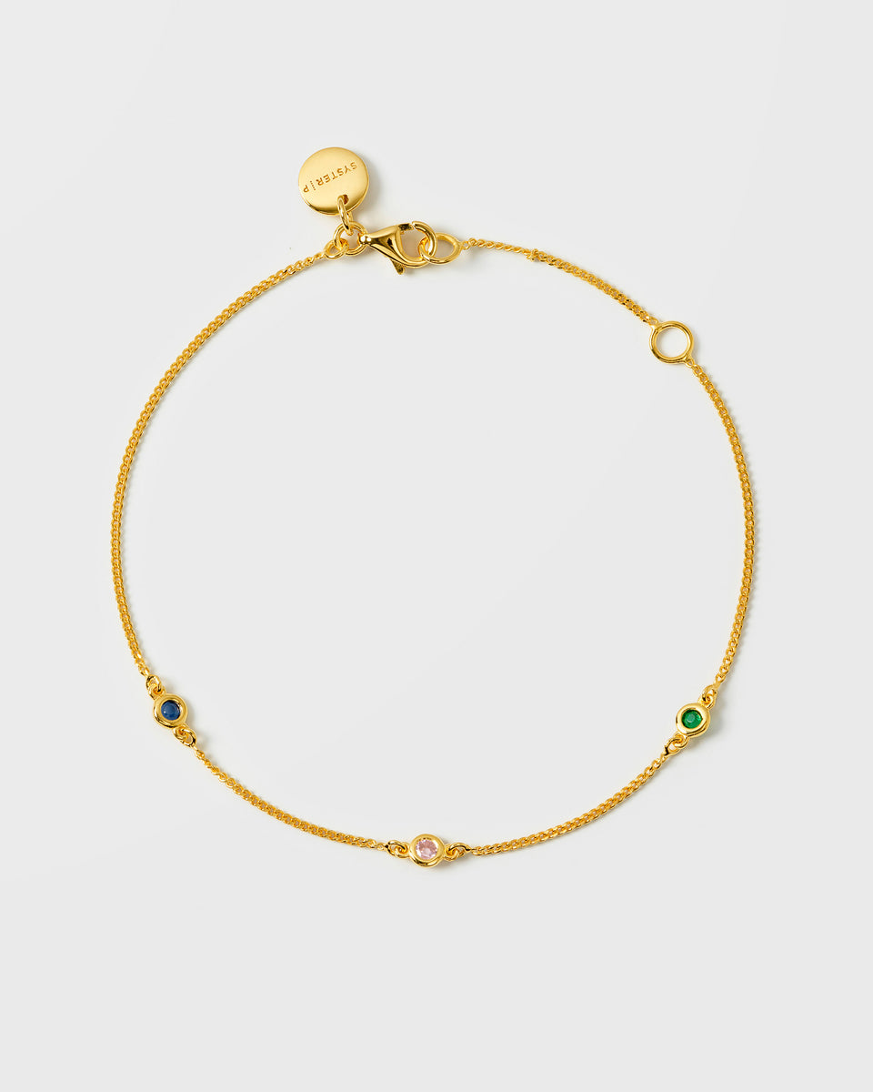 A product shot of the Treasure Shimmer Bracelet in gold, laid out in a circle to display its delicate chain with three multi-coloured faceted zirconias.