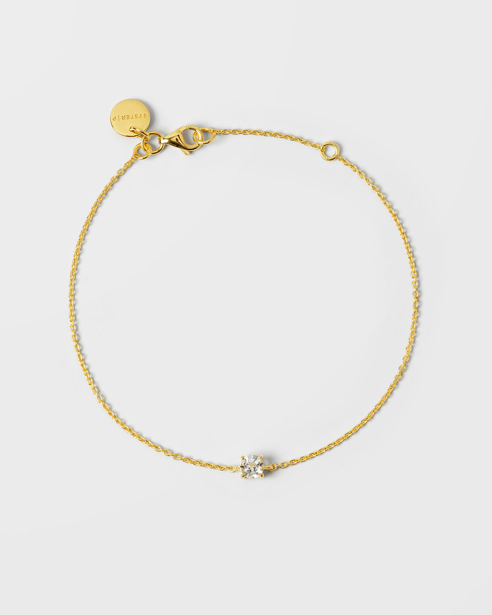 A product shot of the gold Solo Nova Bracelet, laid out in a circle to showcase its fine chain and single clear stone centerpiece.