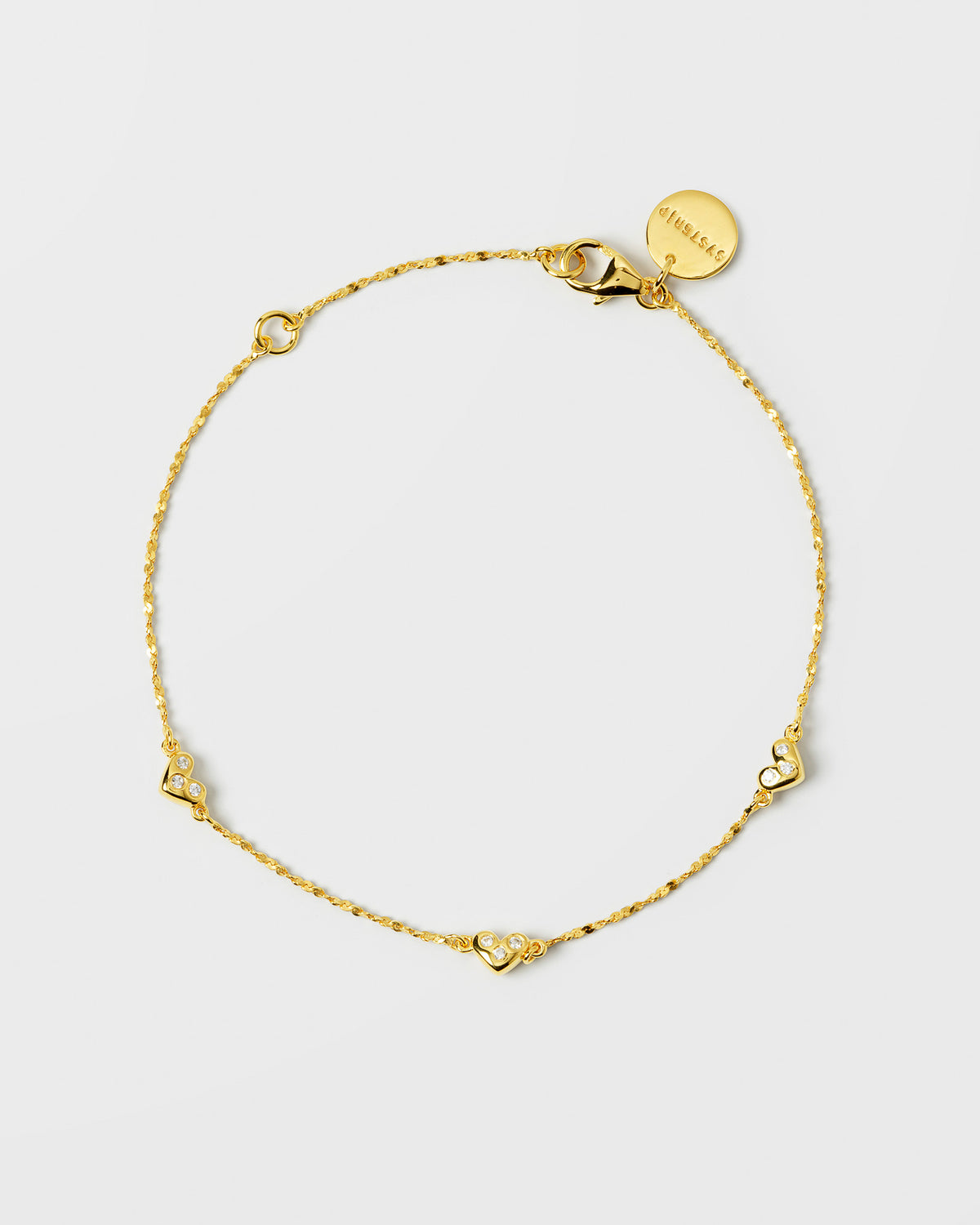 Product shot of the gold Forever Bracelet, laid out to showcase its delicate twisted chain and small heart charms set with sparkling cubic zirconia stones.
