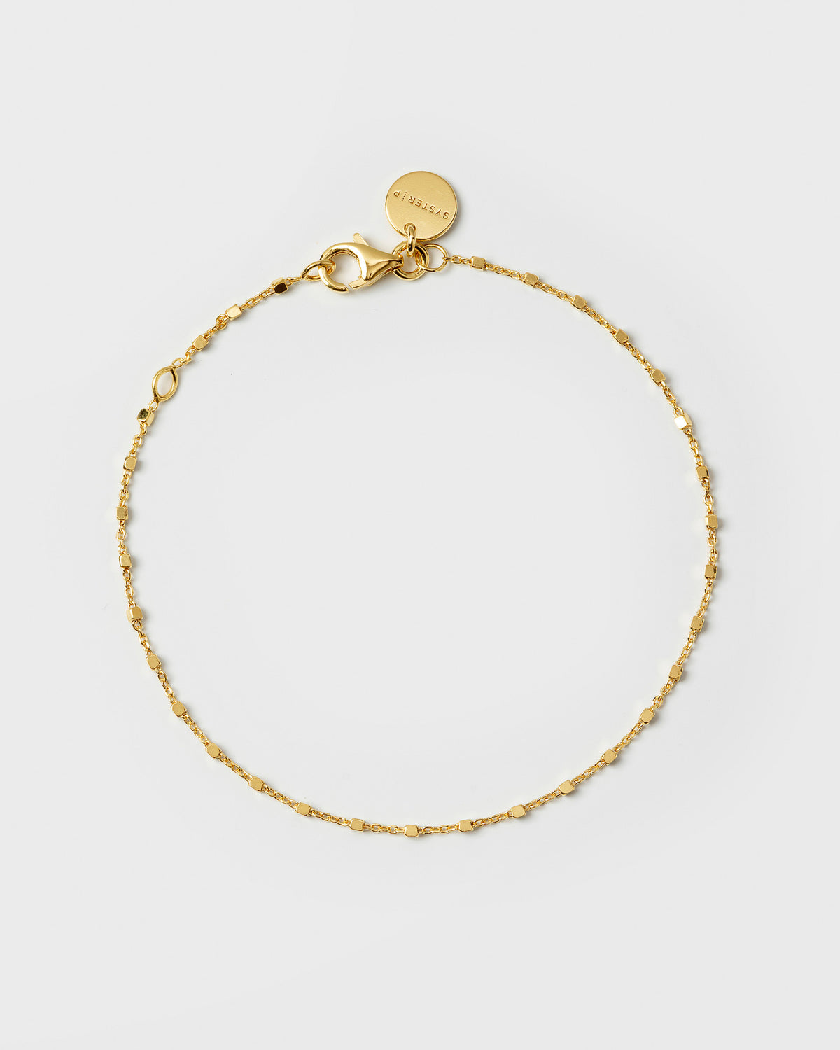 A product shot of the Sheer Station Bracelet in gold, laid out in a circle to display its delicate chain with small, square beads.