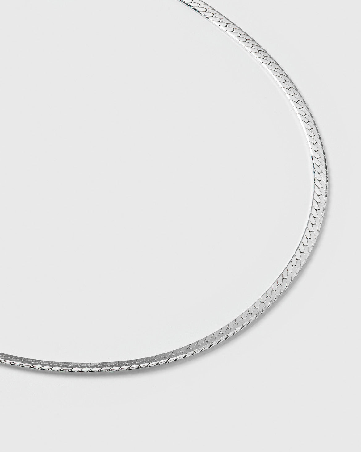 A product shot of the Herringbone Bracelet in silver, laid out in a curve to showcase its smooth, flat, and delicate herringbone chain design.
