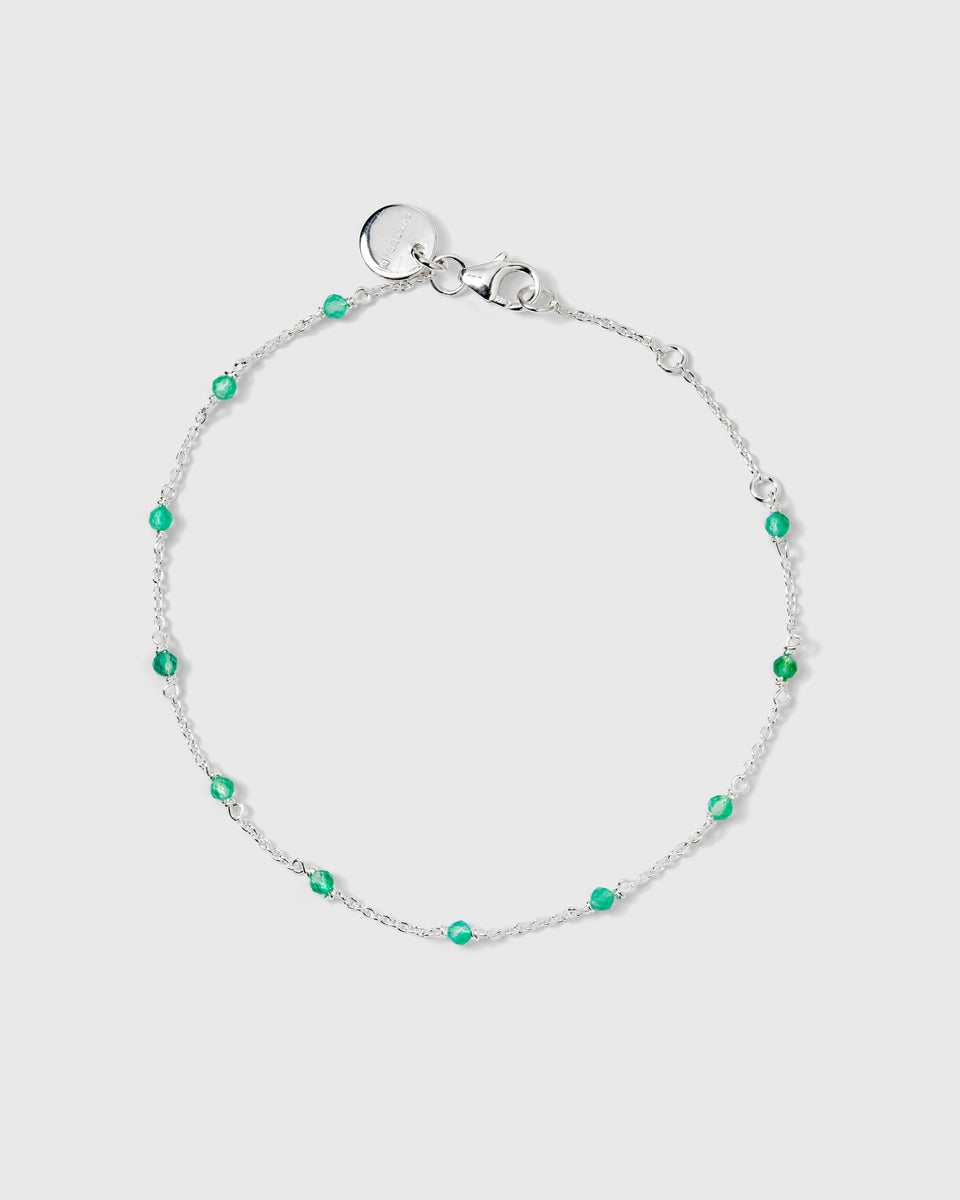 A product shot of the Santa Monica Bracelet in silver, laid out in a circle to display its delicate chain design adorned with small green onyx stones spaced throughout.