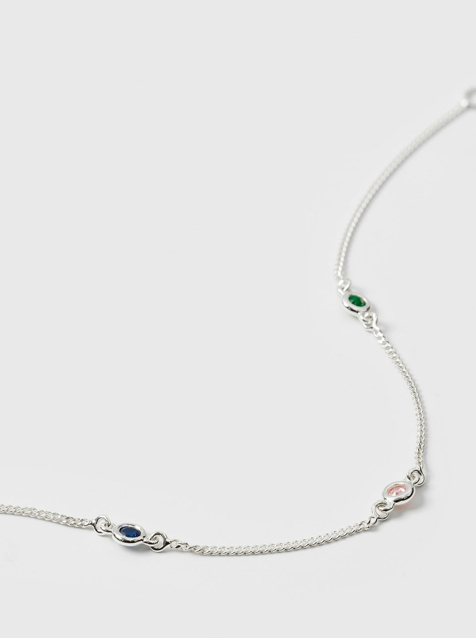 A product shot of the Treasure Shimmer Bracelet in silver, laid out to display its delicate chain design featuring three colourful, faceted zirconias.