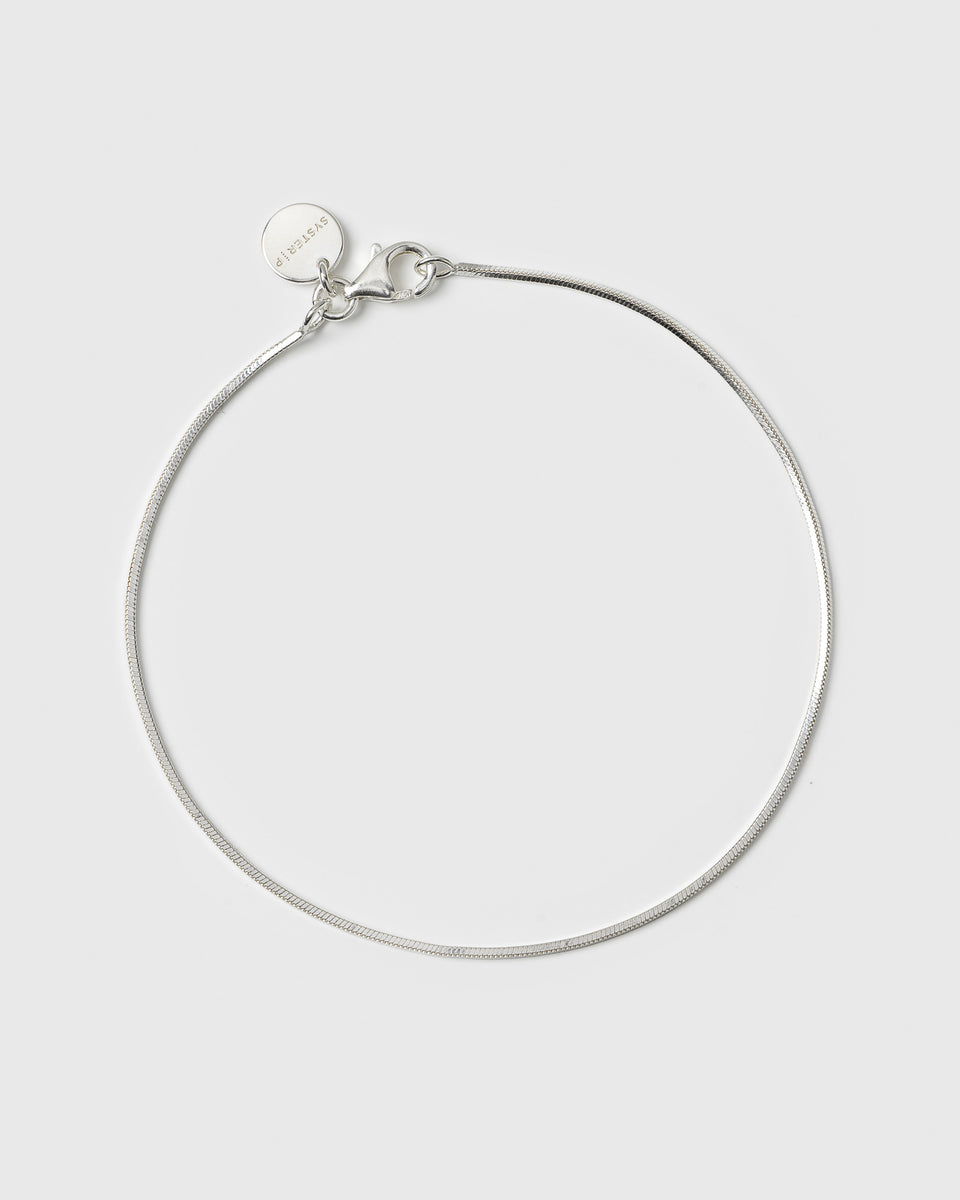 A product shot of the Sheer Mirror Bracelet in silver, laid out in a circle to display its delicate and smooth snake chain design, lobster clasp, and small Syster P branded charm.