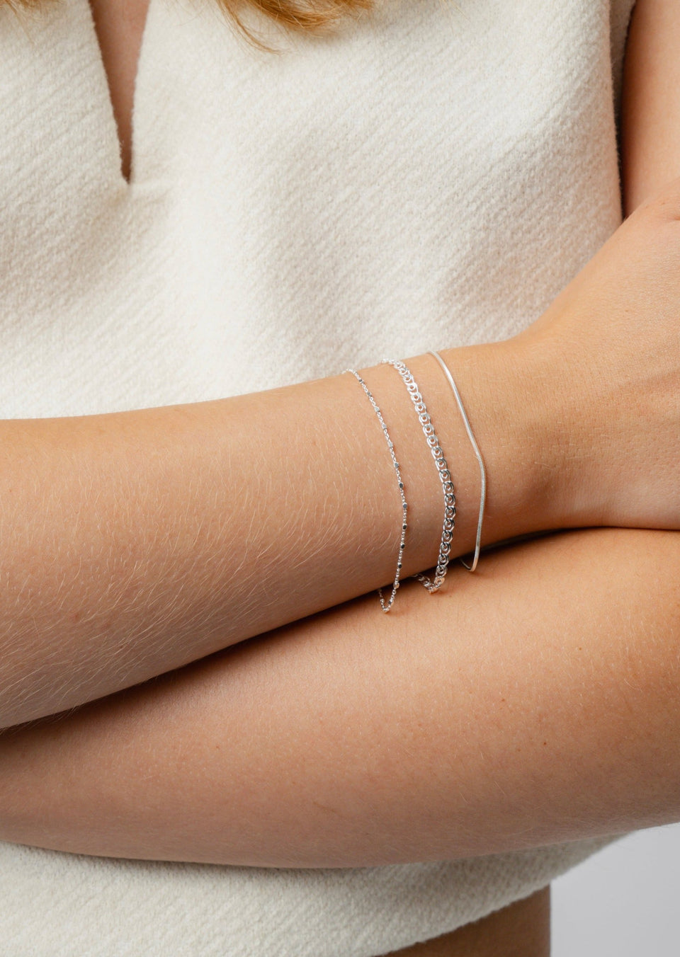 A model wearing the Sheer Love Bracelet in silver, which features a distinctive patterned chain, layered with a fine beaded chain and a sleek snake chain bracelet.