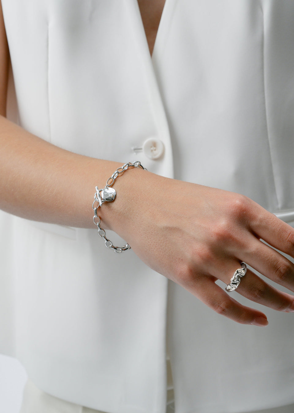 A model wears the Paxton Heavy Bracelet in silver, a chunky link chain with a toggle clasp and a pearl charm. She also wears a textured silver ring on her other hand.