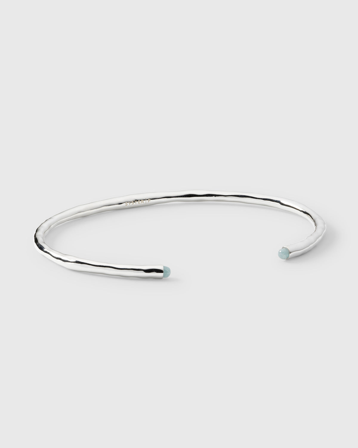 A product shot of the Florentina Bangle in silver, showcasing its hammered surface and the two pale blue aquamarine stones at its open ends.