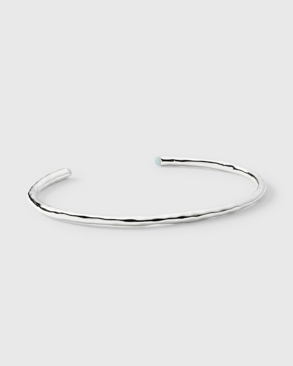 A product shot of the Florentina Bangle in silver, an open cuff with a hammered texture, featuring a small aquamarine stone at each end.