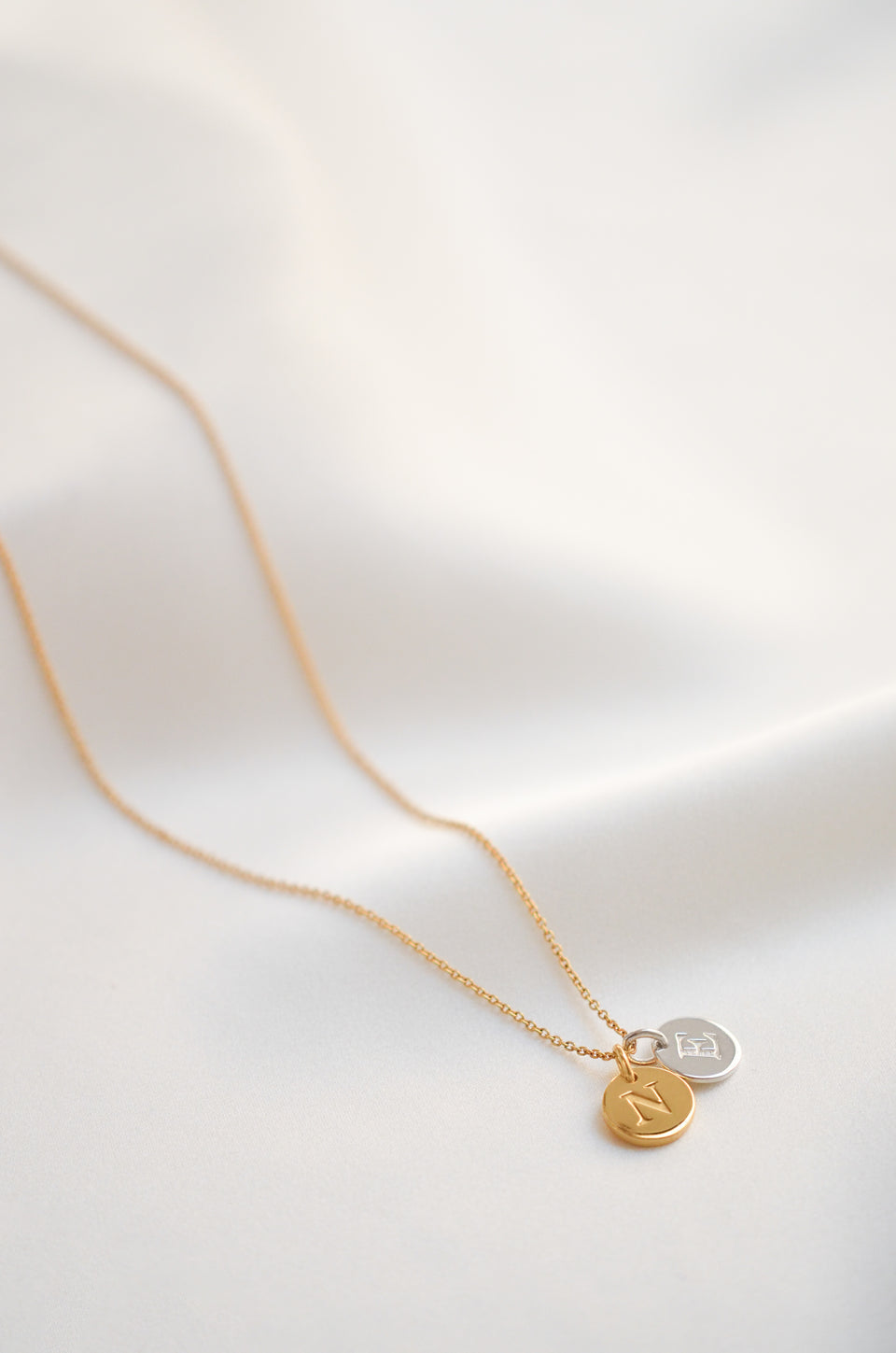 A product shot of the Beloved Short Oval Chain in gold, styled with a round gold 'N' initial pendant and a round silver 'E' initial pendant.