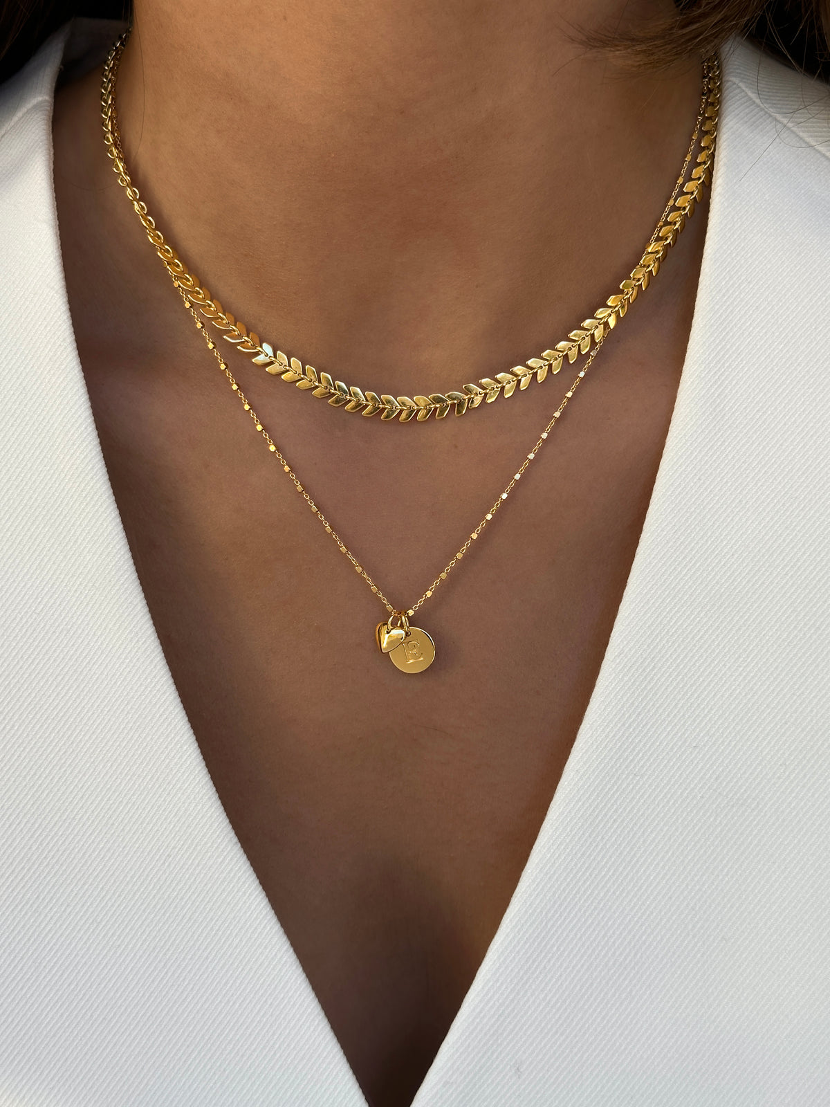 Modell som bär två guld halsband med två berlocker.