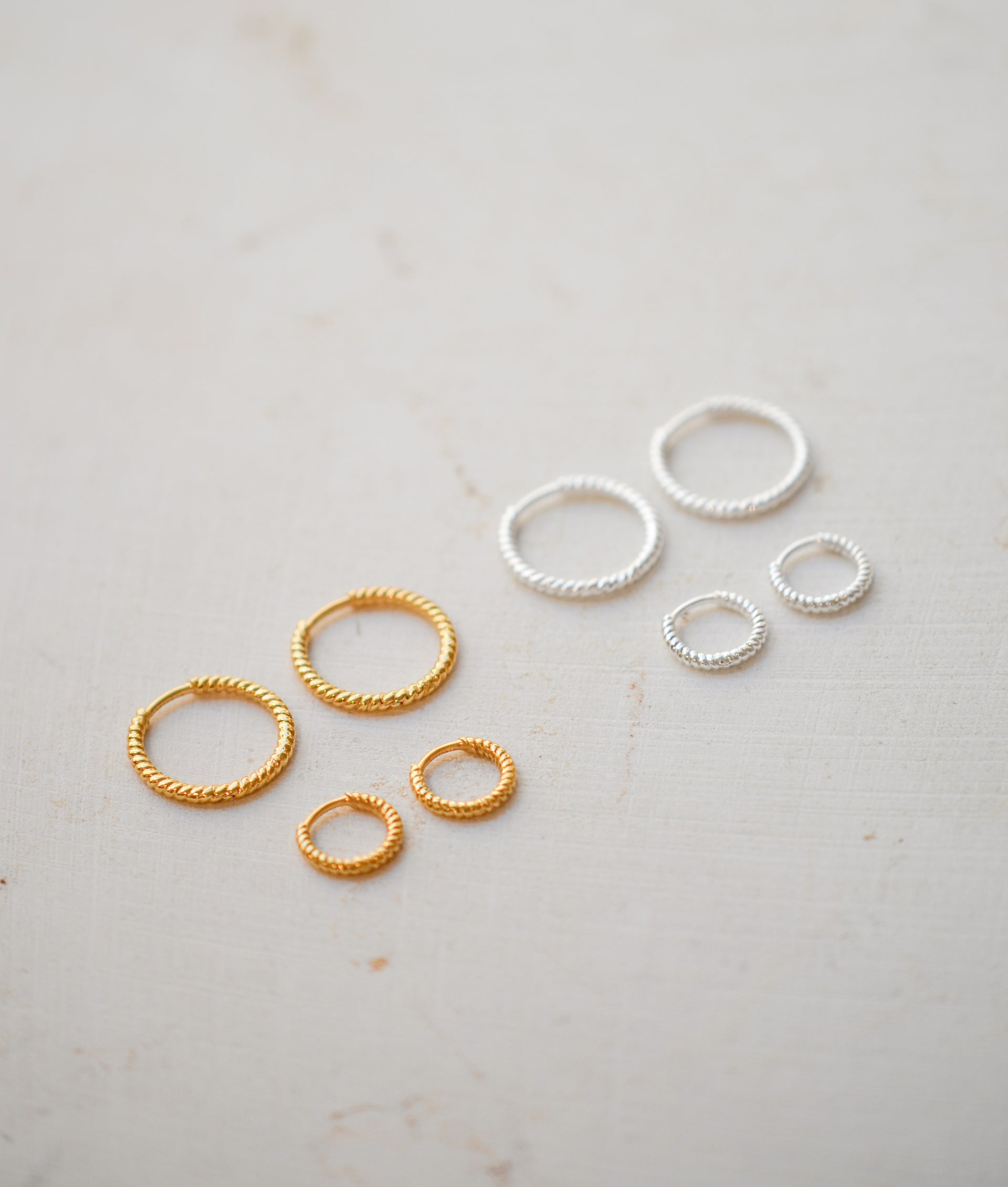 Gold hoops in two different sizes next to silver hoops in two different sizes
