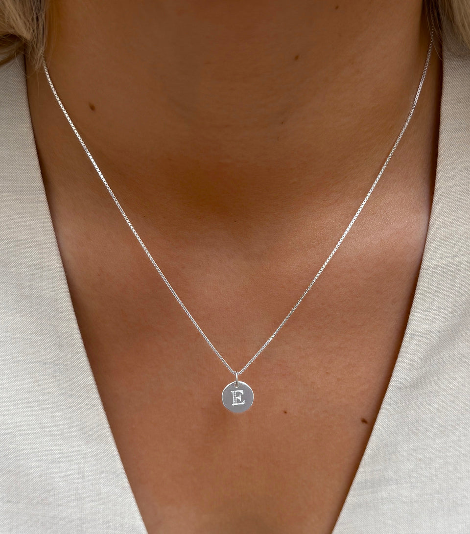A close-up shot of a model wearing the Syster P Beloved Mini Letter 'E' pendant on a silver short box chain necklace.