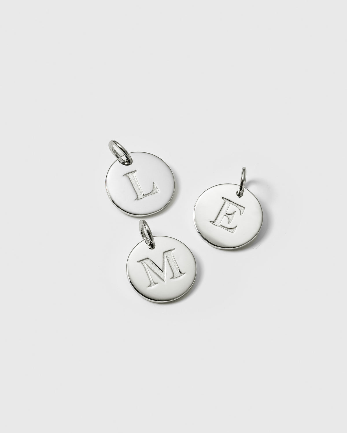 A product shot of three Beloved Big Letter Silver charms, featuring the letters L, M, and E engraved on the round pendants.