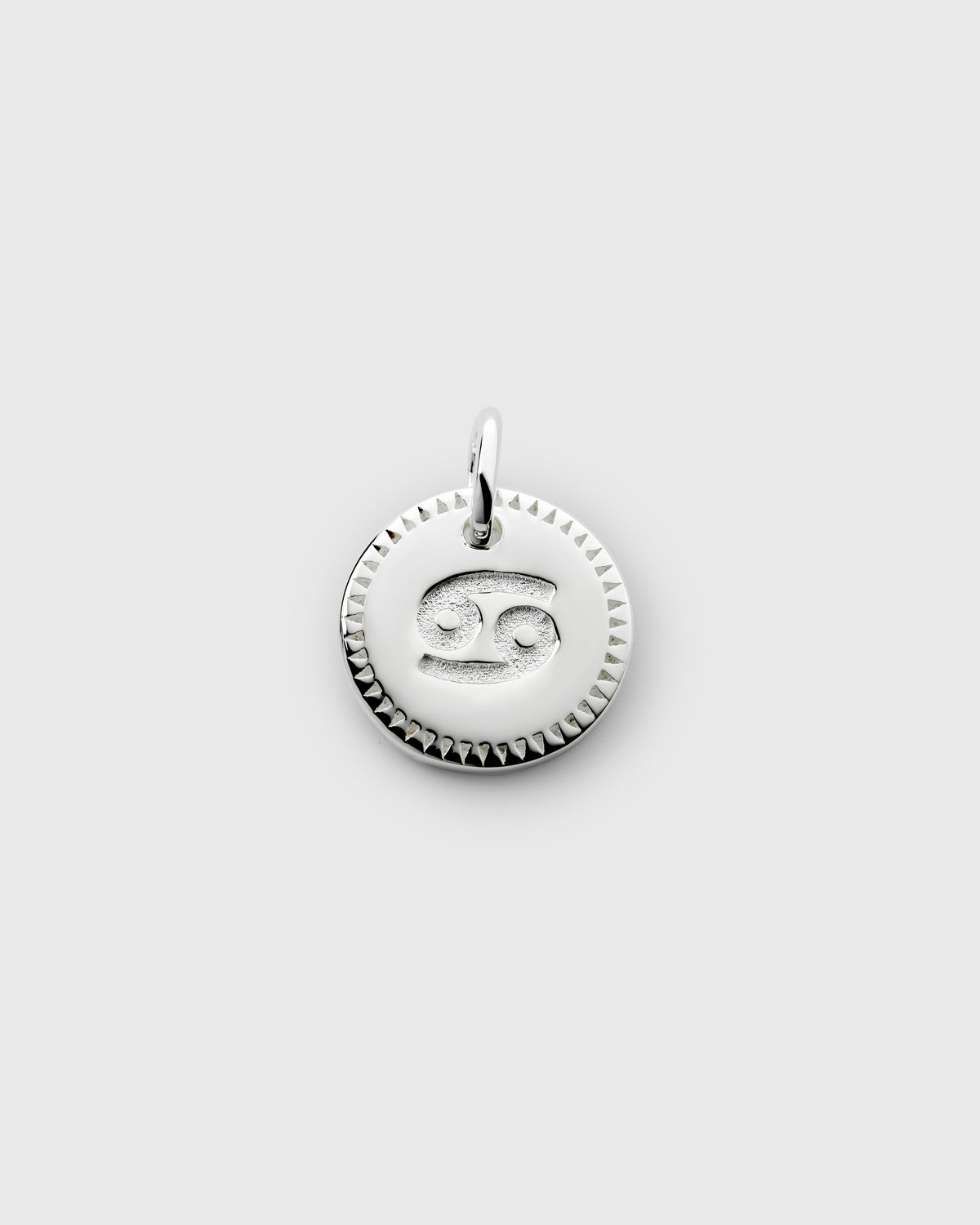 A product shot of the Beloved Zodie Pendant in silver, featuring the zodiac sign Cancer engraved in the center of the round charm, which is framed by a decorative triangular-patterned border.