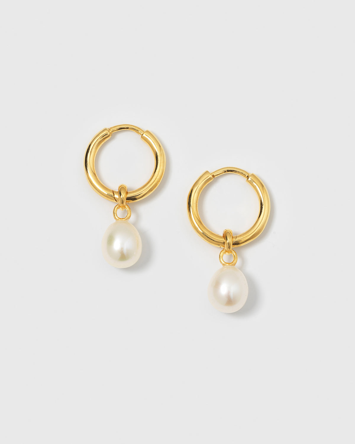 A product shot of the Treasure Pearl Hoops in gold, highlighting the classic design of a simple hoop with a dangling freshwater pearl.