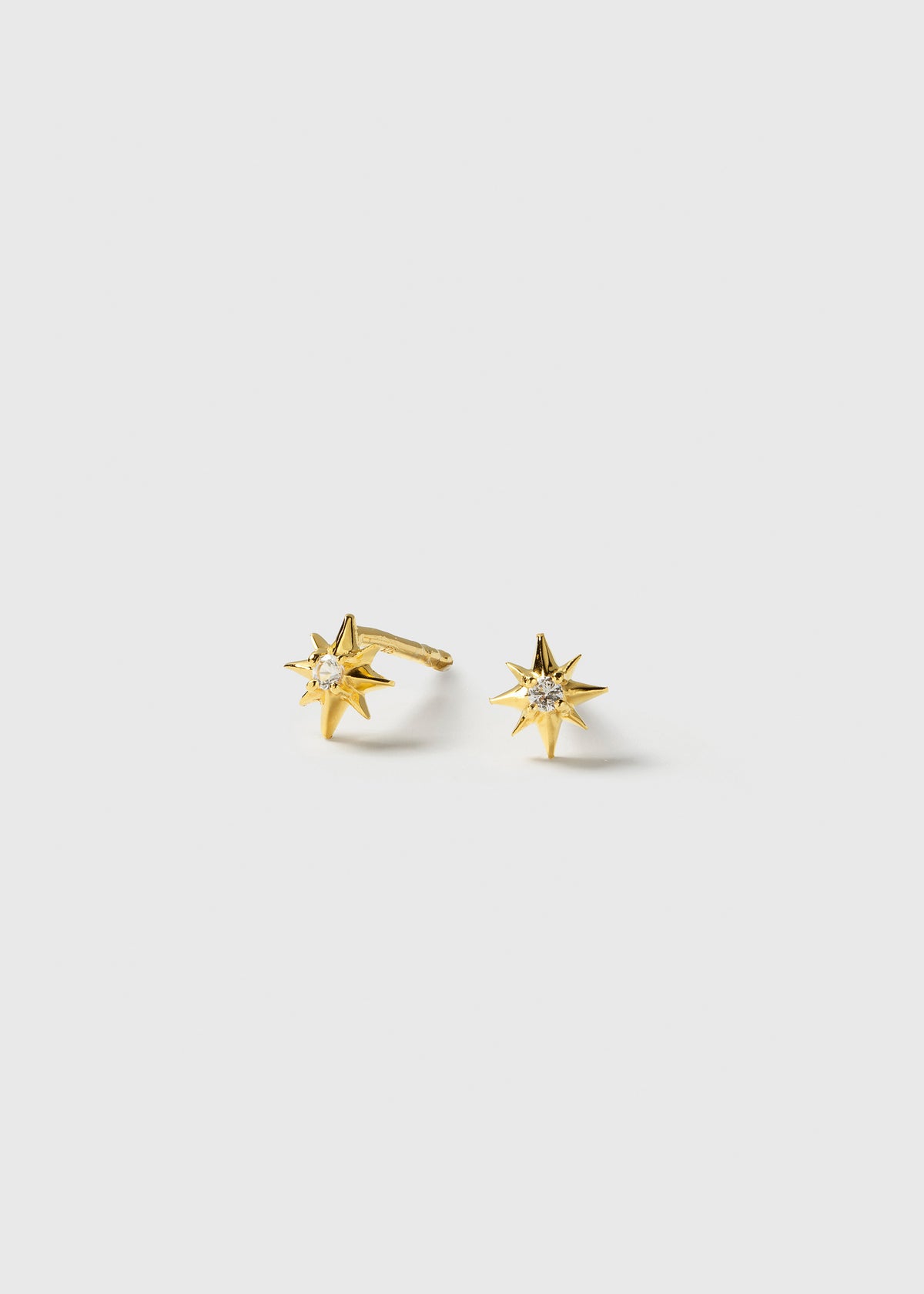 A product shot of the North Star Studs Gold, displaying the pair of earrings which are designed as eight-pointed stars, each with a small, clear crystal at its center.