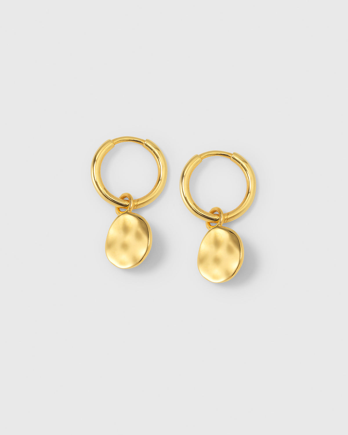 A product shot of the Minimalistica Hammered Earrings in gold, featuring small hoops with dangling pendants that have a hammered surface.