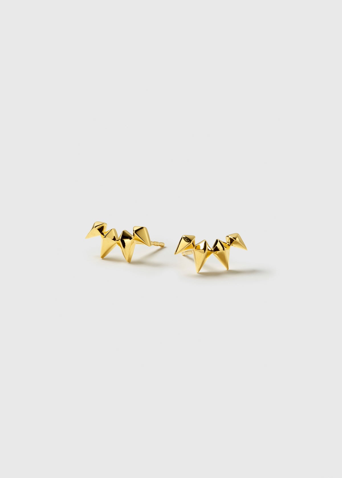 A product shot of the Uma Climber Earrings in gold, laid out to display their design of a curved row of small spikes.