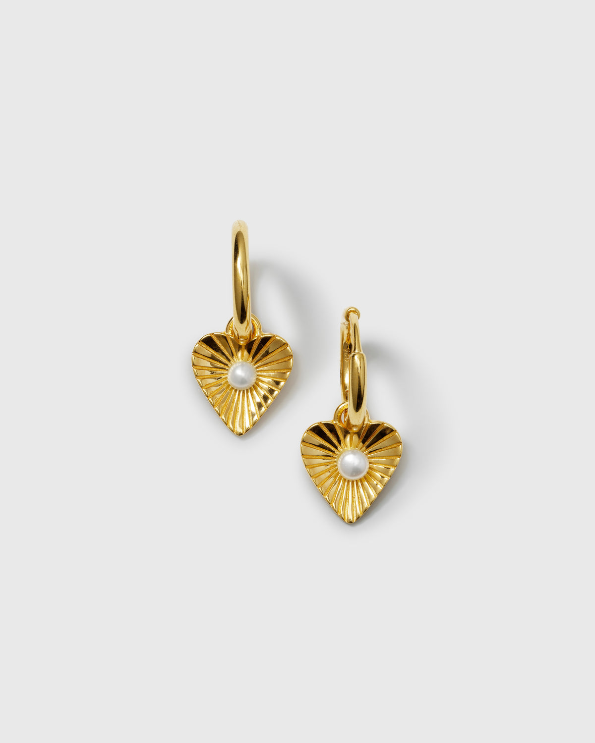 A product shot of the Aurelia Earrings in gold, showcasing the hoop design with a dangling heart-shaped pendant, which features a grooved texture and a central freshwater pearl.