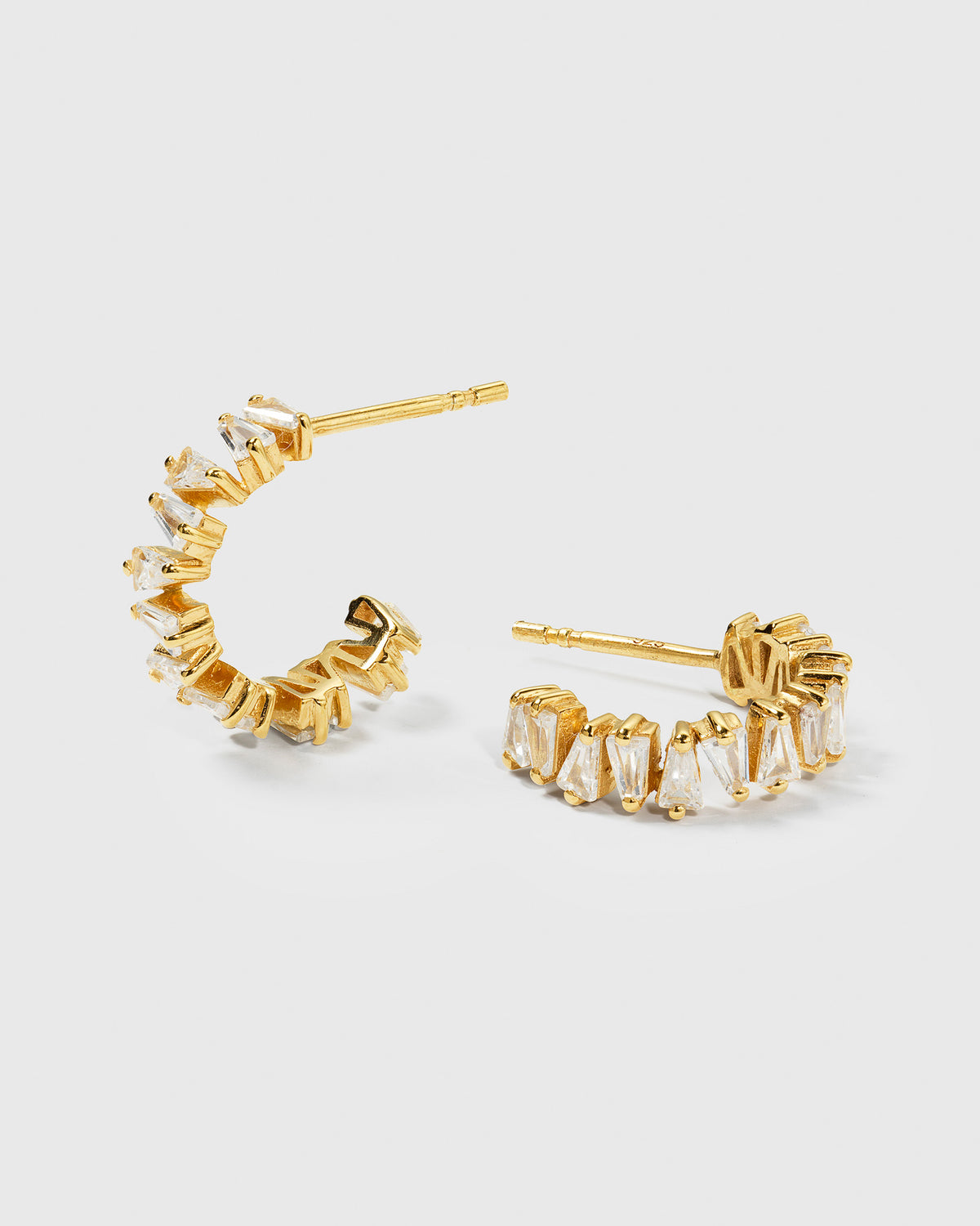 A product shot of the Iggy Earrings in gold, featuring their open hoop design set with sparkling, tapered baguette-cut cubic zirconias.