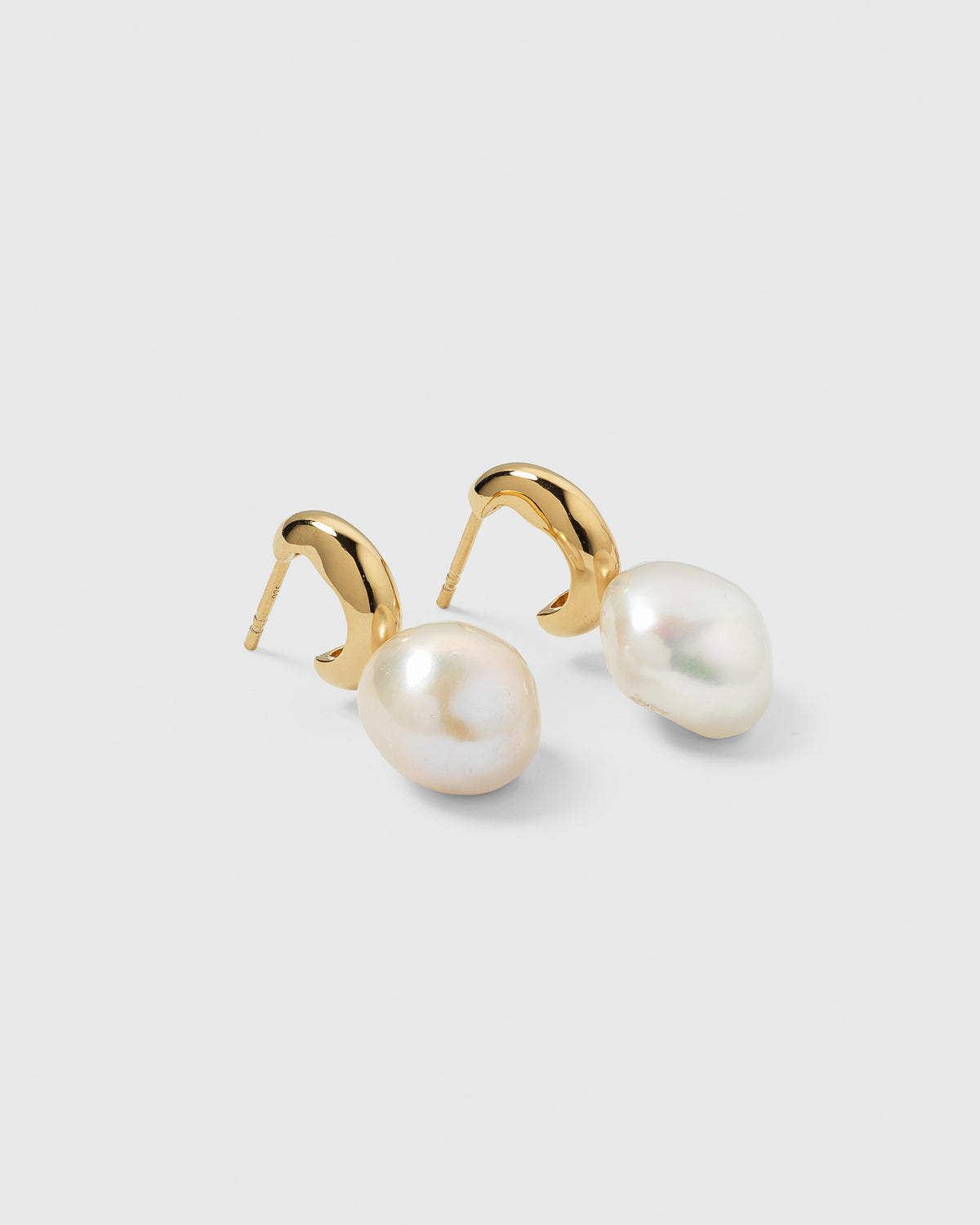 A close-up of the gold Paxton earrings, a pair of earrings with a unique curved design and a large, lustrous baroque freshwater pearl hanging from each.