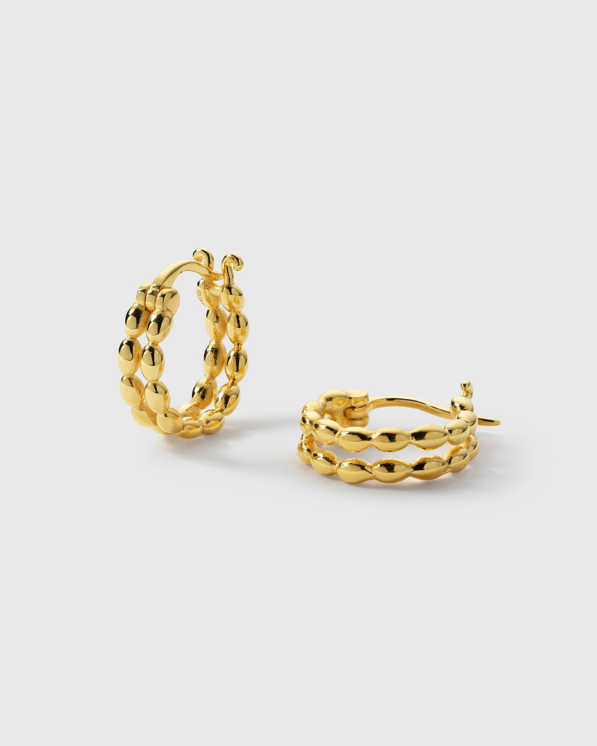 A product shot of the Lunetta Earrings in gold, showcasing their unique design where two parallel hoops are linked by a pattern of small ovals.