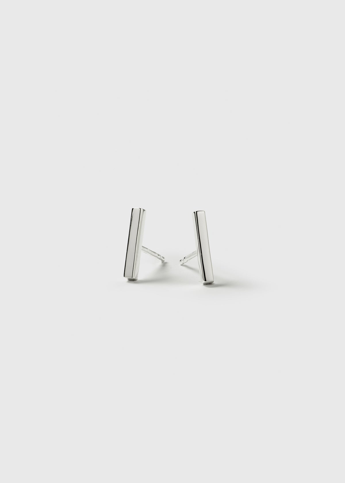 A product shot of the Strict Bar Earrings in silver, showing the pair of simple, minimalist bar-shaped studs.