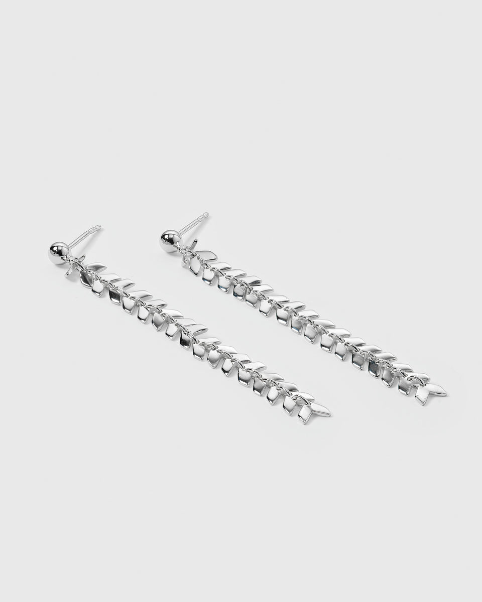 A product shot of the Layers Olivia Earrings in silver, laid out to display their long, dangling design of interconnected, small leaf-like charms.