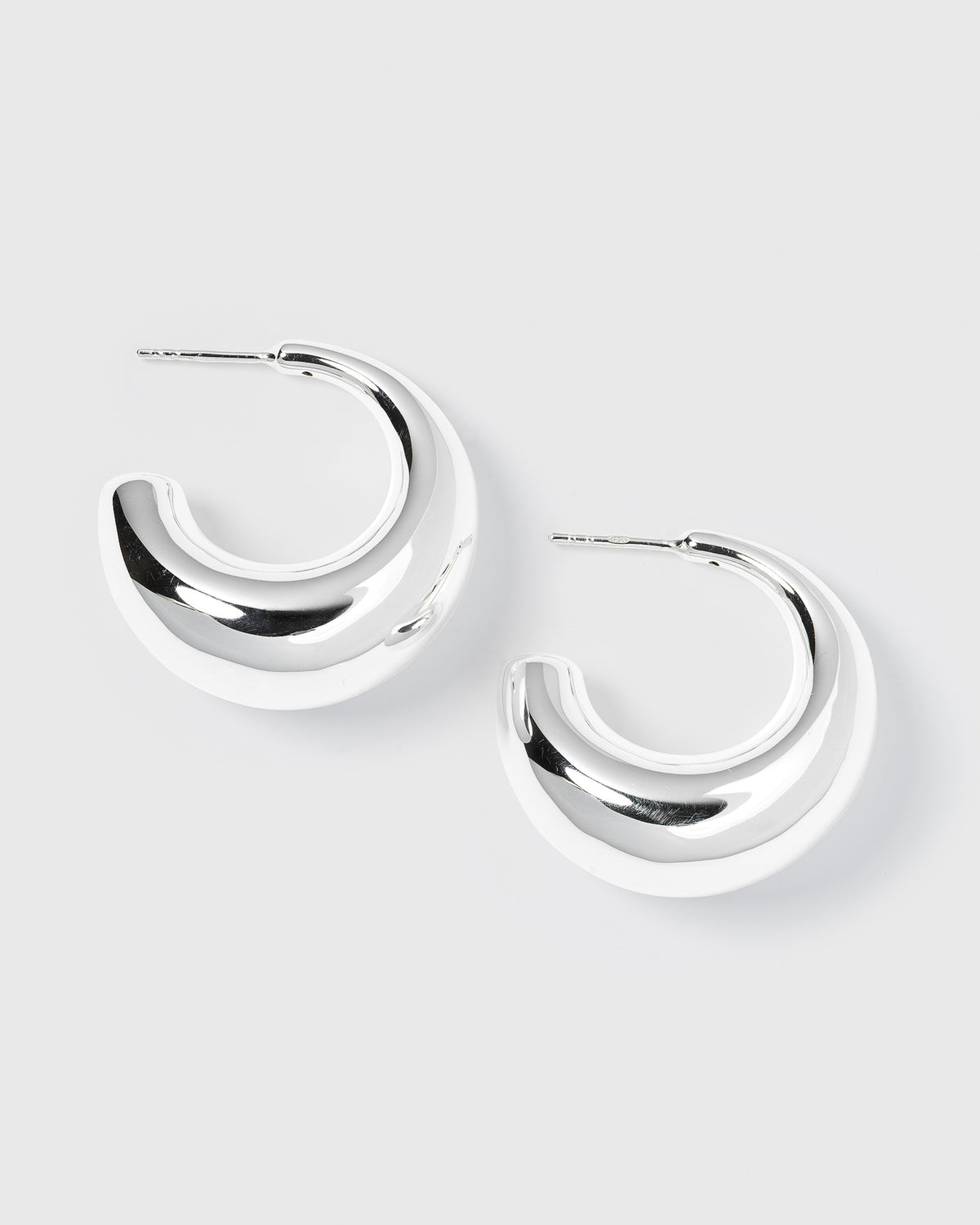 A product shot of the Bolded Earrings in silver, laid out to showcase their unique, chunky and sculptural hoop design.