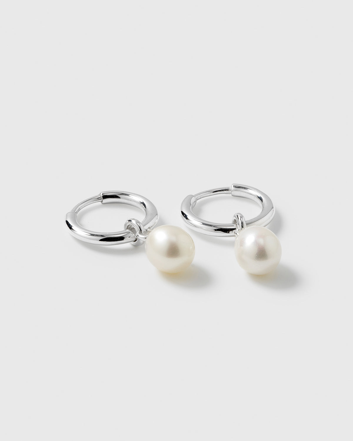 A product shot of the Treasure Pearl Hoops Silver, featuring a pair of small silver hoops with dangling freshwater pearls.