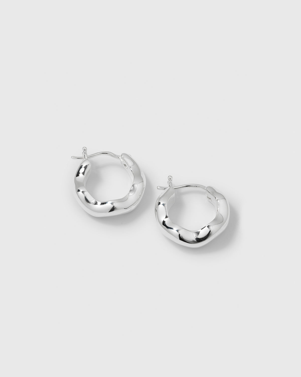 A product shot of the Bolded Wavy Earrings in silver, displaying the pair of shiny hoops and their distinct, irregular wavy design.