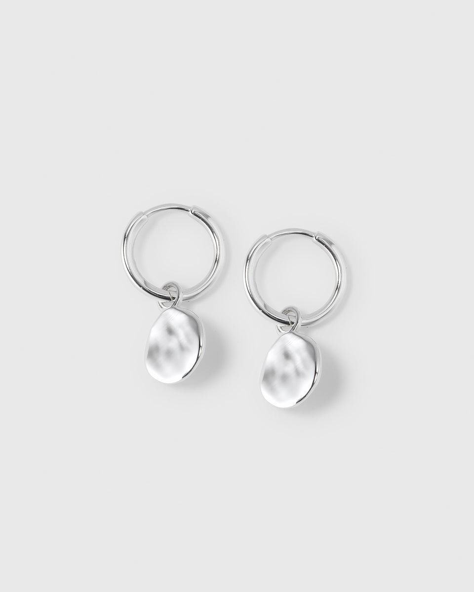 A product shot of the Minimalistica Hammered Earrings in silver, featuring a pair of small hoops, each with a dangling pendant with a hammered surface.