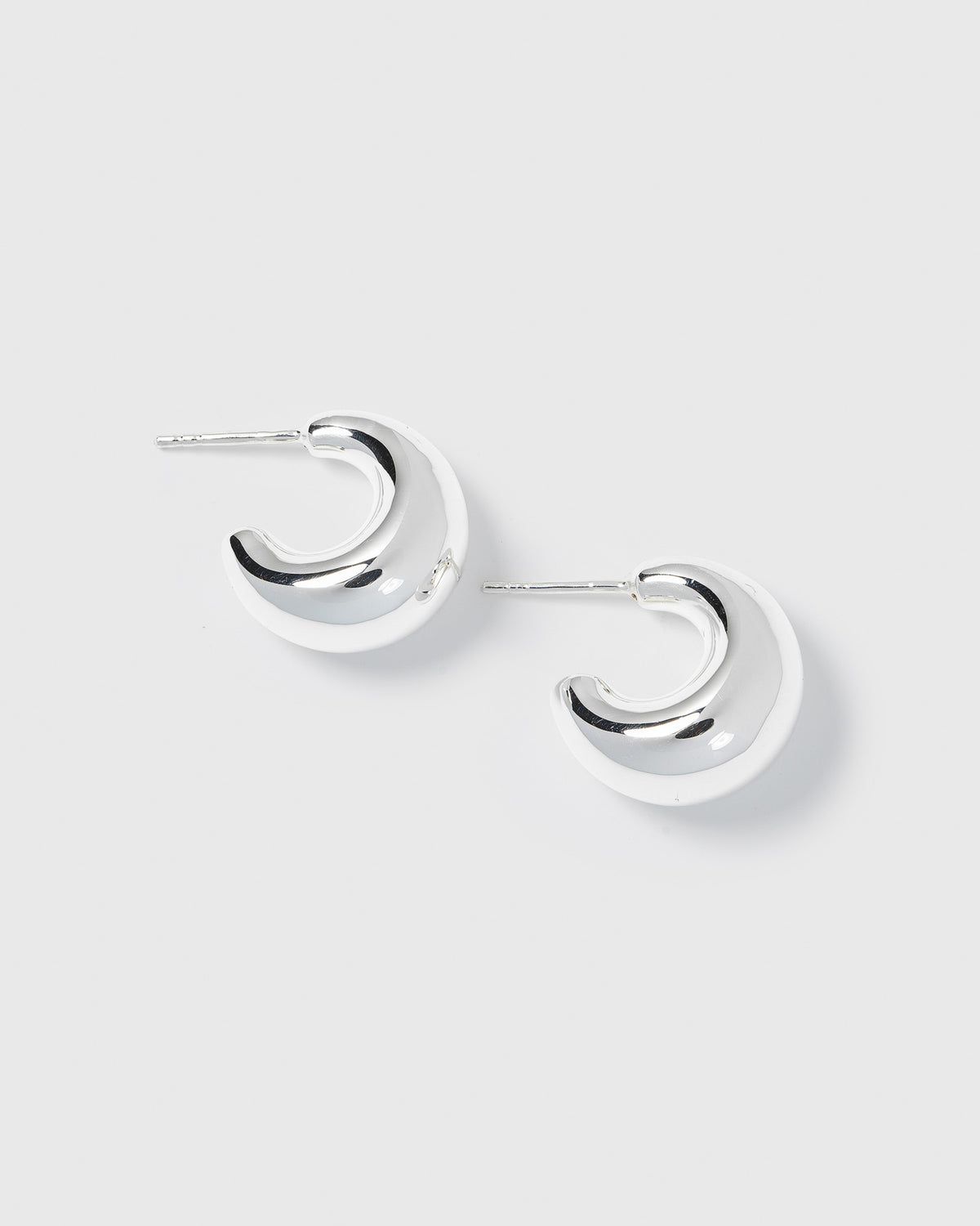 A product shot of the Bolded Little Sis Earrings in silver, showcasing their chunky and polished crescent hoop design.