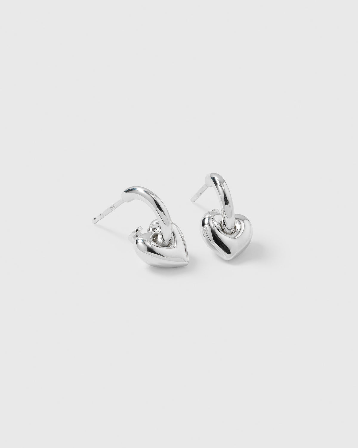A pair of La La Love Fat Heart Earrings in silver, featuring small hoops with chunky, puffed heart pendants.