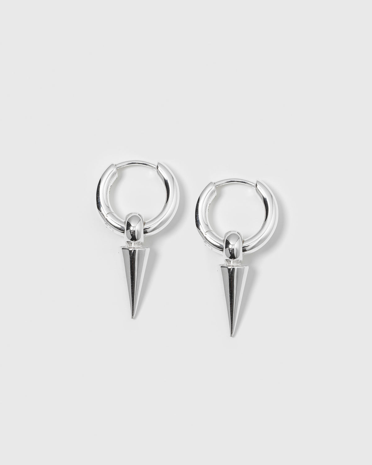 A product shot of the Juno Hoops in silver, featuring a pair of small hoop earrings with dangling, cone-shaped spike pendants.