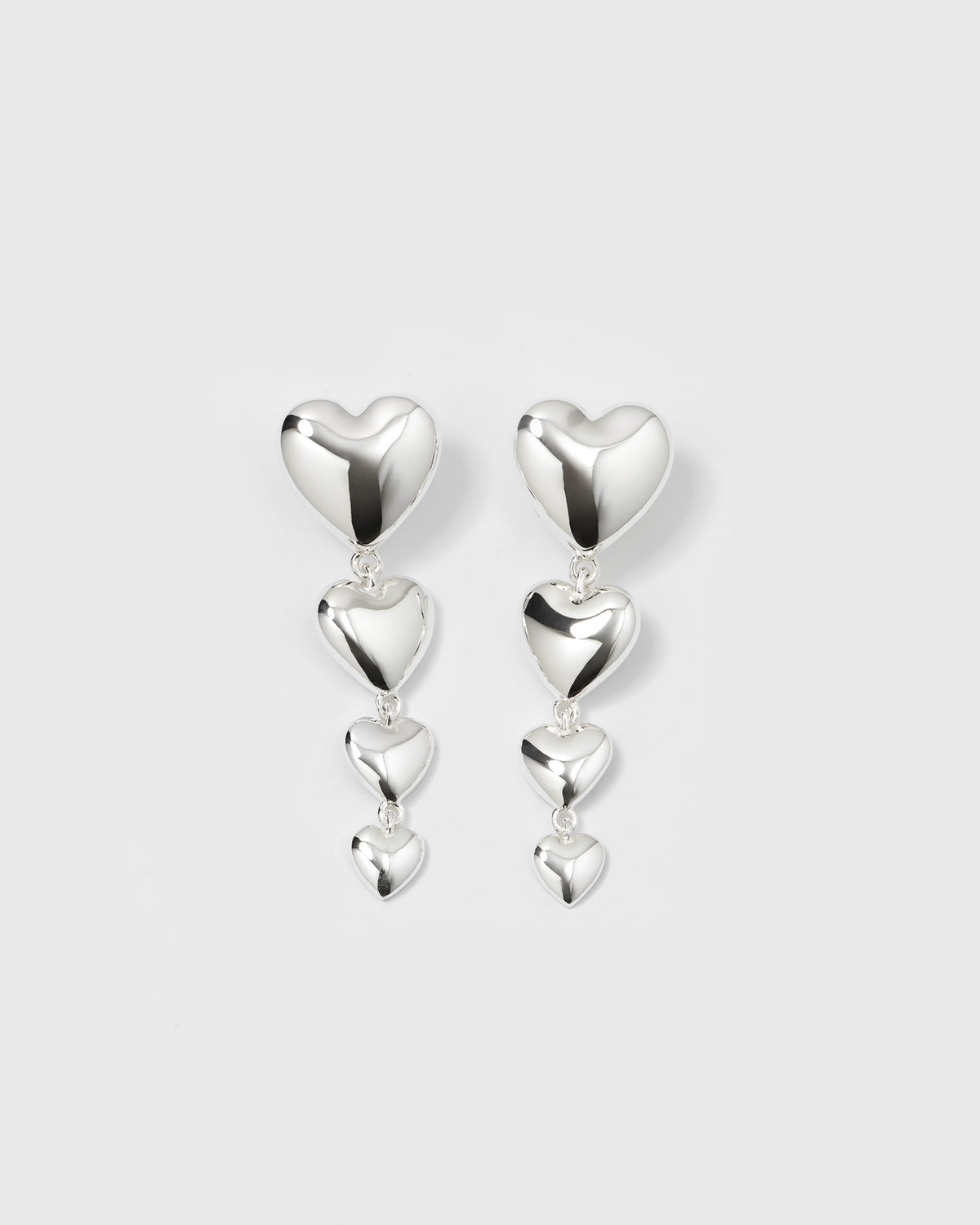 A product shot of the Darling Earrings in silver, which feature a long pendant formed by four cascading, bold hearts.