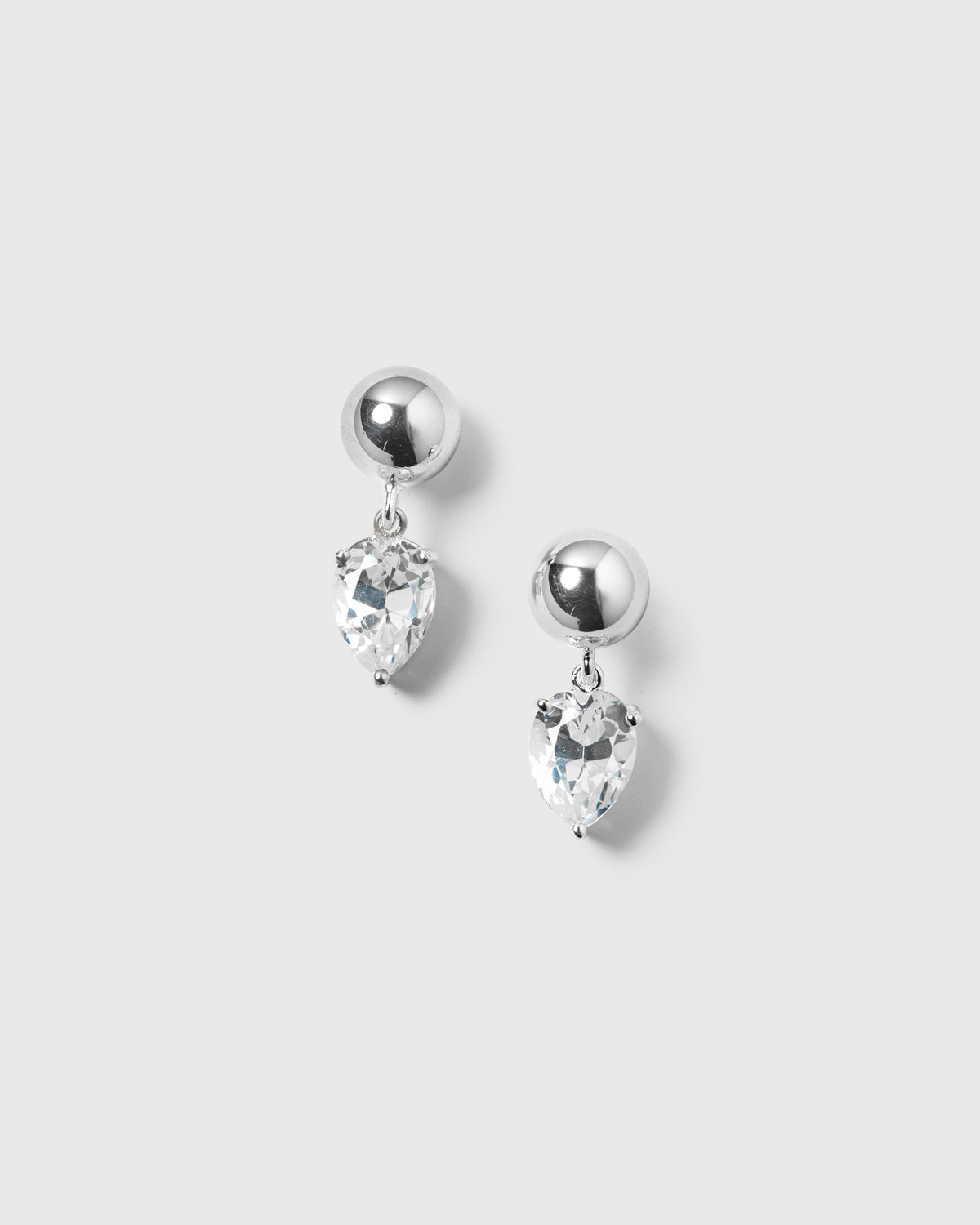 A product shot of the Katie Earrings in silver, featuring polished ball studs with a dangling drop-shaped cubic zirconia.