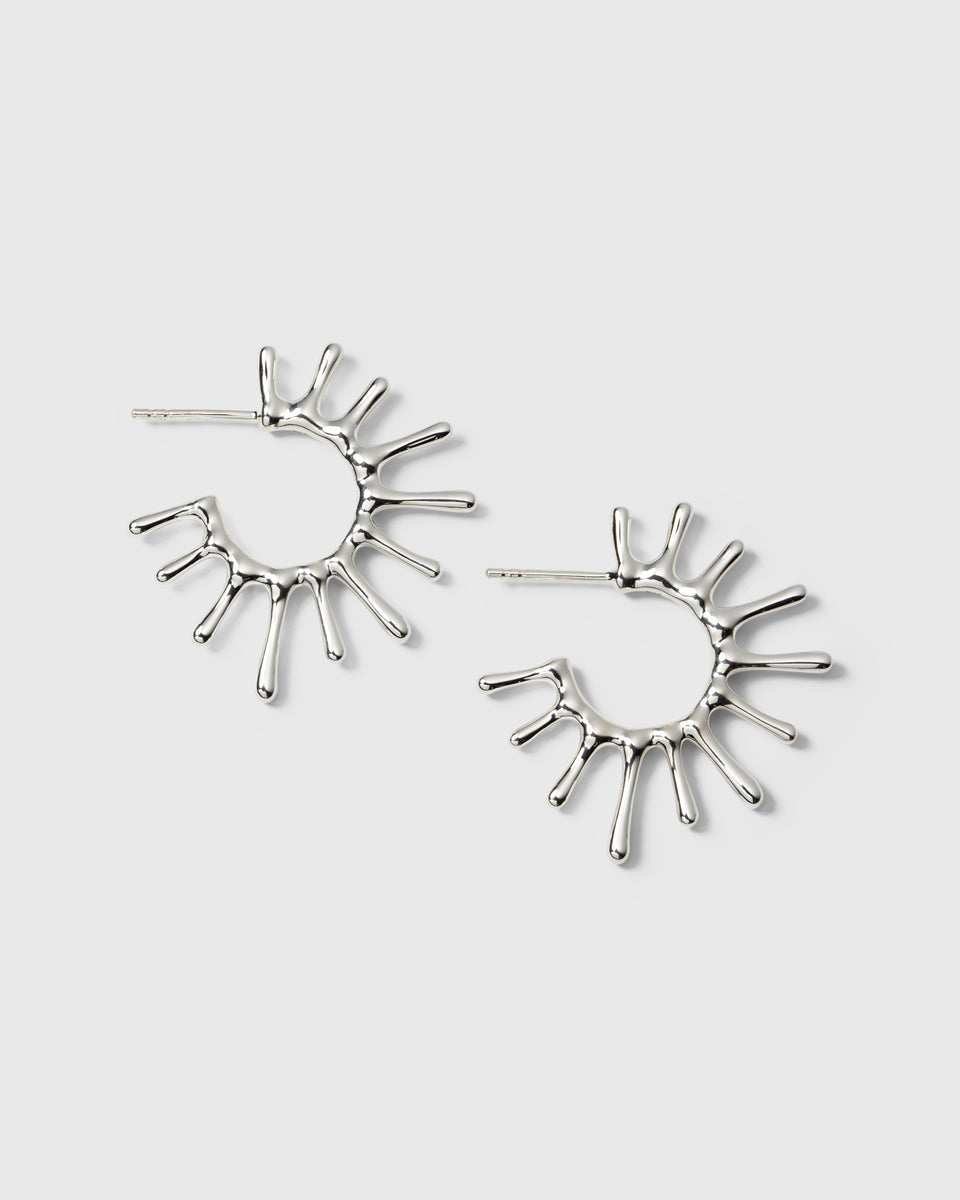 A product shot of the Florentina Big Earrings in silver, showcasing their unique hoop design inspired by the sun, with irregular rays extending from the band.
