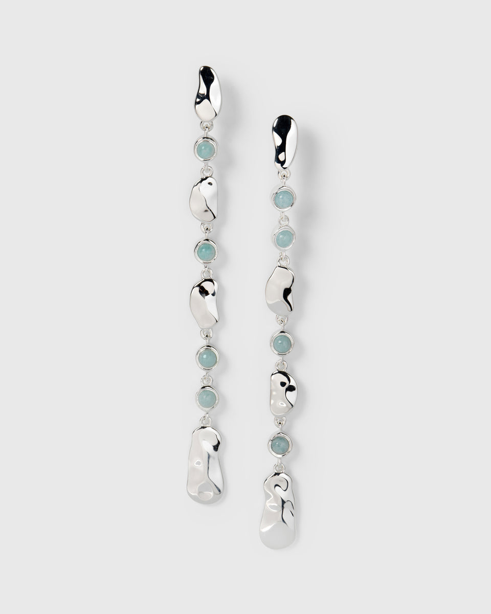 A product shot of the Florentina Long Earrings in silver, showing their long, dangling design of hammered silver plates alternating with round aquamarine stones.