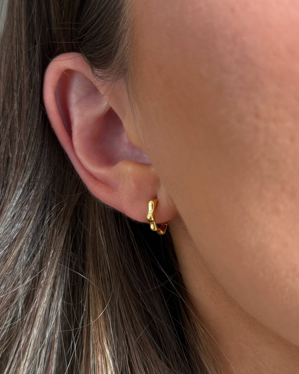 A close-up of a small gold hoop earring with a wavy pattern.
