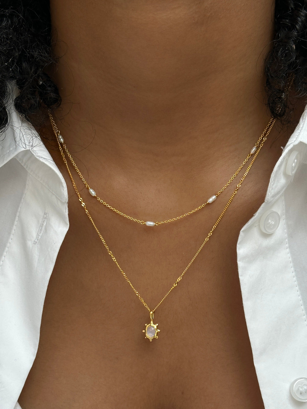 A close-up on a model's neck shows a layered look, featuring the gold Treasure Multi Pearl Necklace with its delicate freshwater pearls, styled with the Florentina Necklace with a moonstone pendant.