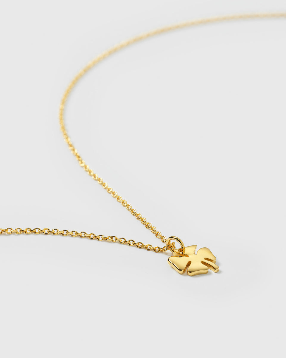 A close-up product shot of the Bring Me Luck Necklace in gold, focusing on its four-leaf clover pendant attached to a delicate chain.