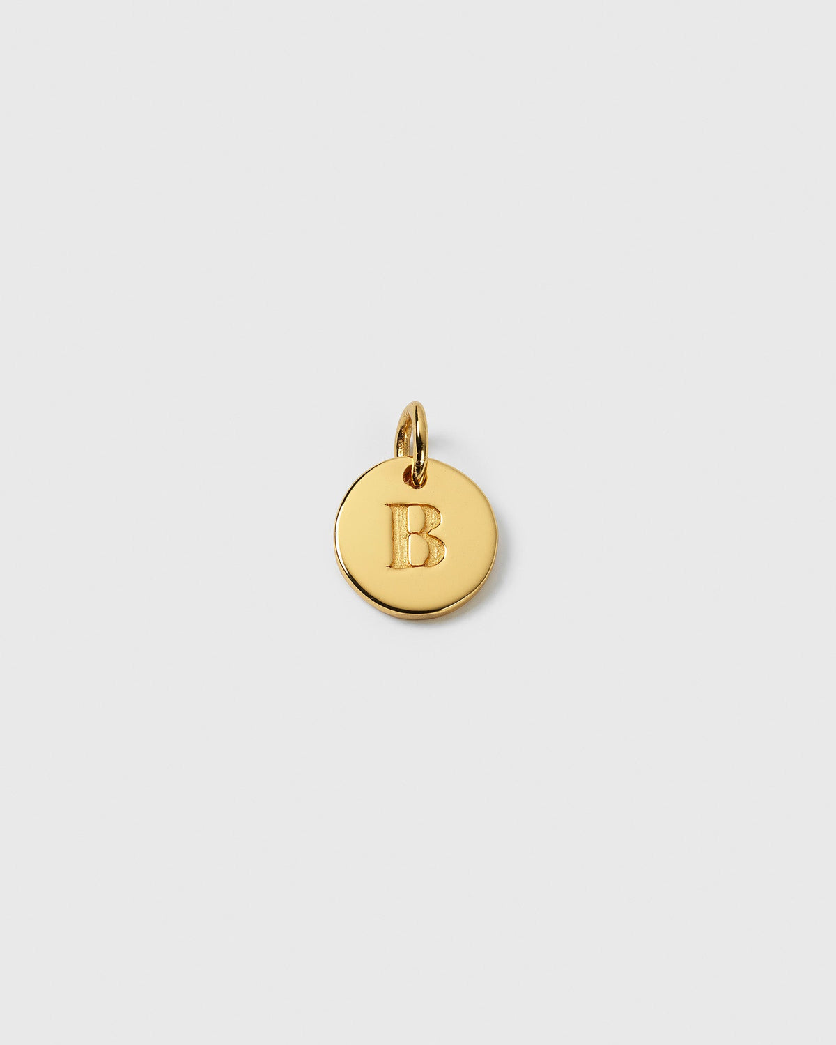 A close-up product shot of the gold Beloved Mini Letter pendant, a small round charm with the letter 'B' engraved on it.