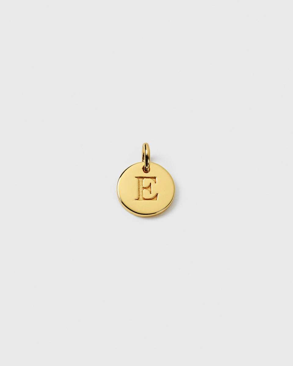 A close-up of the Beloved Mini Letter Gold charm, showing the letter 'E' engraved onto the small, round pendant.