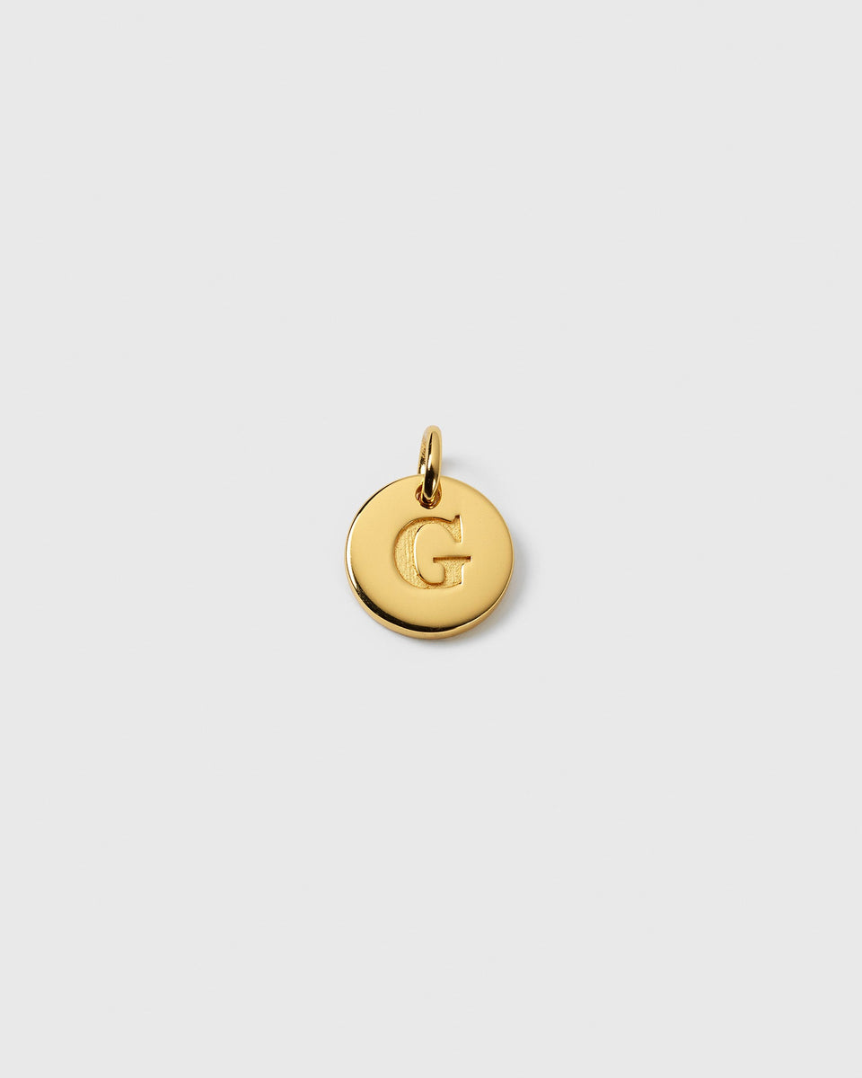 A product shot of the Beloved Mini Letter Gold charm, featuring the letter 'G' engraved onto the circular pendant.