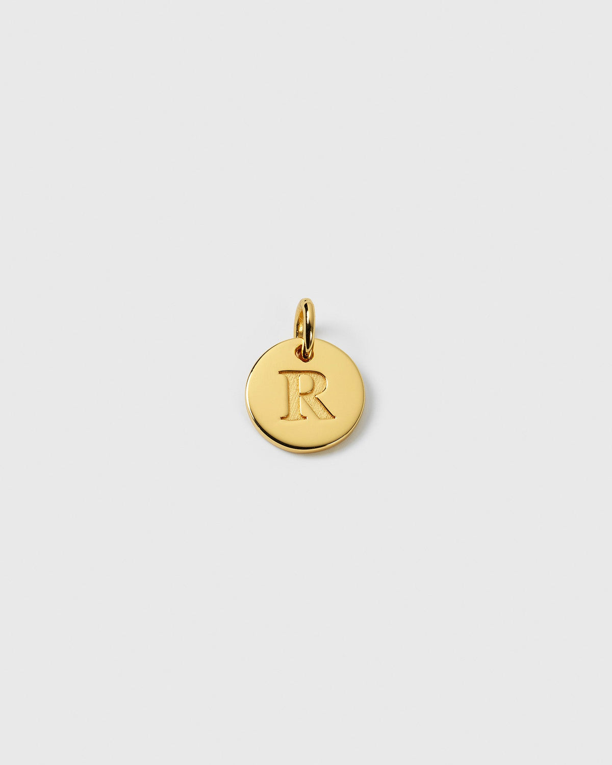 A product shot of the Beloved Mini Letter Gold pendant, featuring a small, round charm with the letter 'R' engraved on it.