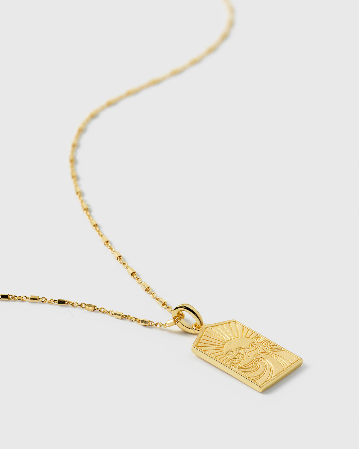 A product shot of the Lucky Coin Keep Dreaming Necklace in gold, featuring its delicate chain and a rectangular pendant engraved with a paradise scene of a sun over waves.